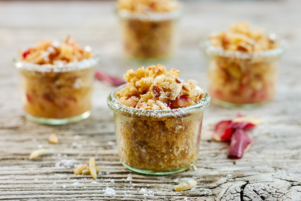 Vier hausgemachte Apfelcrumbles in Gl&auml;sern auf rustikalem Holztisch