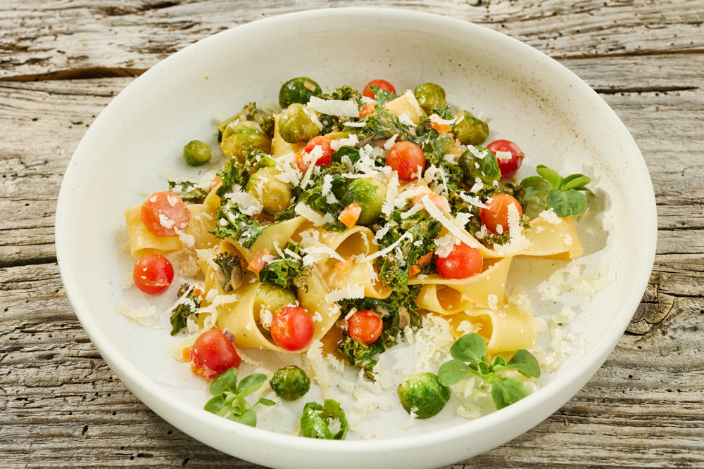 Winterliche Gem&uuml;se-Pasta mit Parmesan und frischen Kr&auml;utern auf rustikalem Holztisch