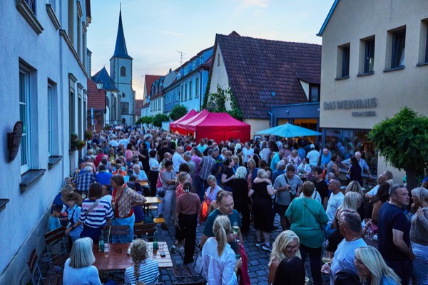 Ha&szlig;furter Lange Nacht, belebter Marktplatz mit Besuchern unter roten und blauen Sonnenschirmen, Kirche im Hintergrund, Foto: Oliver Giel