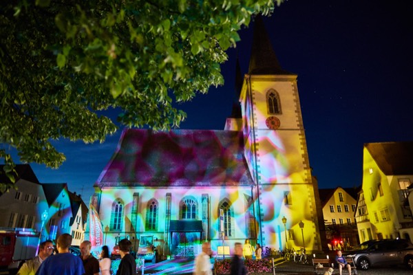 Kirche mit farbenfroher Lichtprojektion bei Nacht, Ha&szlig;furter Lange Nacht, Besucher im Vordergrund, Foto: Oliver Giel