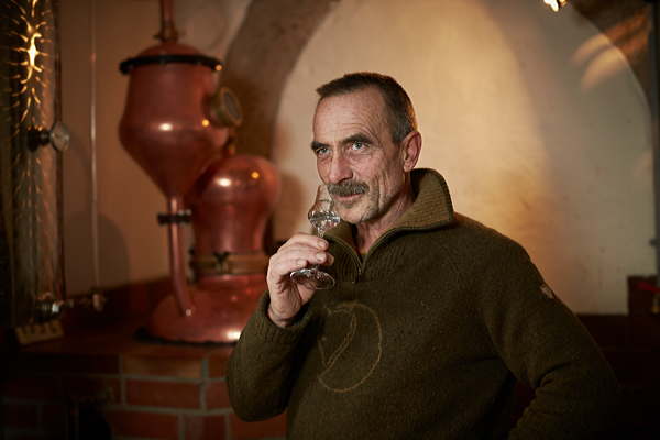 Mann mit Schnapsglas vor kupferner Destillieranlage in einer Brennerei