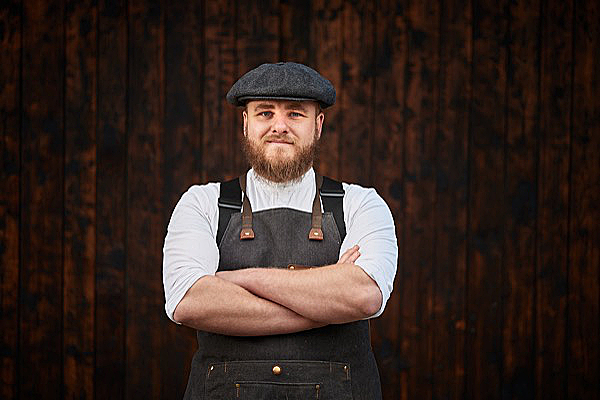 Mann mit Sch&uuml;rze und Flatcap vor Holzwand &ndash; Frankenz&uuml;nder