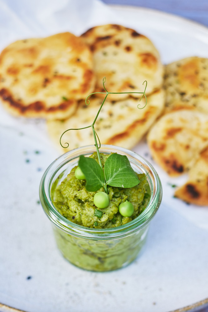 Erbsenhummus im Glas mit Erbsenranke garniert, serviert mit Fladenbrot auf Teller